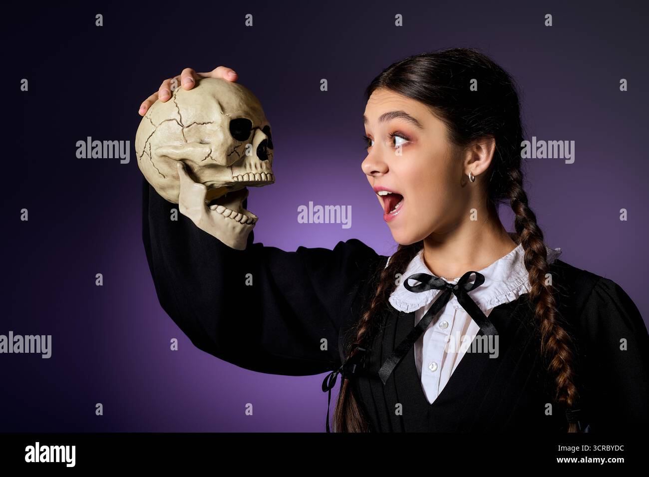Una ragazza con trecce indossa un abito gotico, con gioia tenendo in mano un teschio per il divertimento di Halloween. Foto Stock