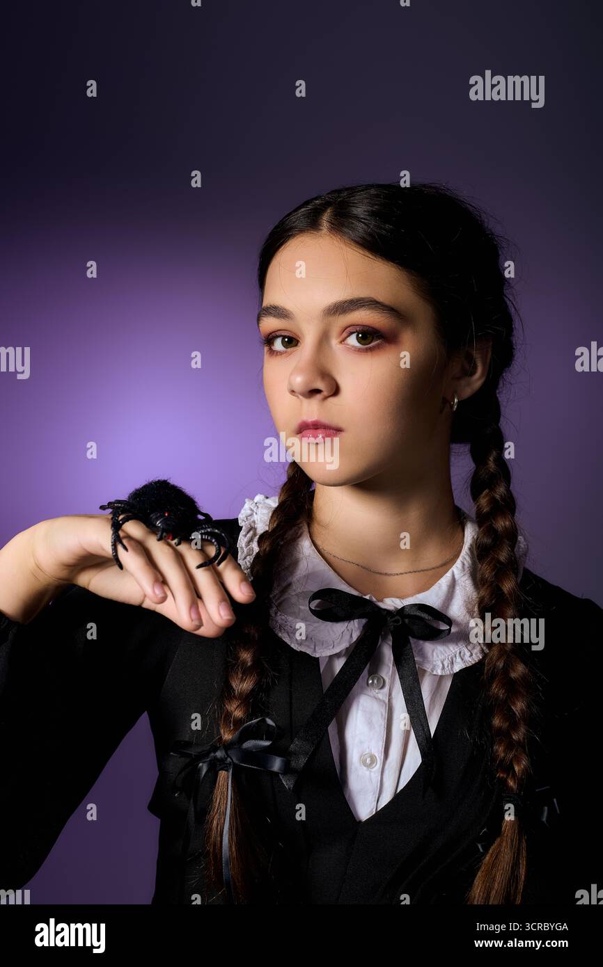 Bambino vestito come un personaggio gotico del mercoledì con trecce, che mostra un ragno per il divertimento di Halloween. Foto Stock