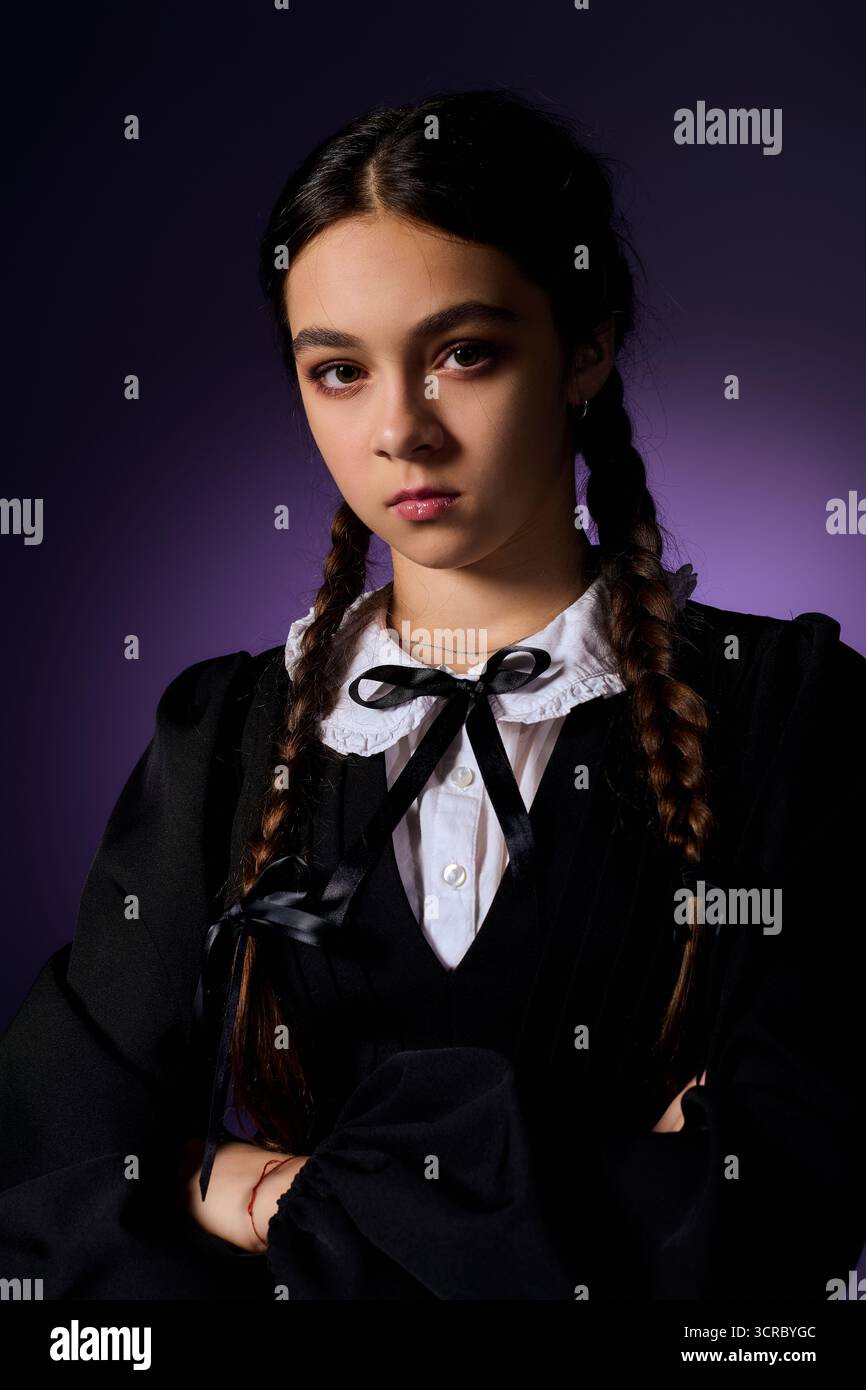 Una ragazza con trecce si posa in un abito gotico, incarnando il personaggio di mercoledì per Halloween. Foto Stock
