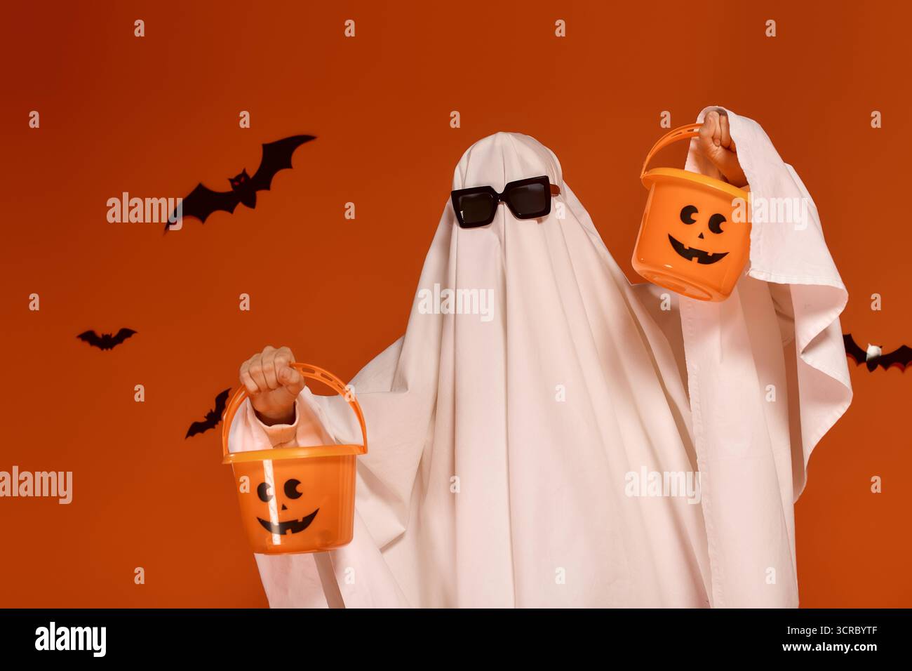 Un bambino giocoso in costume da fantasma regala secchi di caramelle arancioni, celebrando con gioia Halloween. Foto Stock
