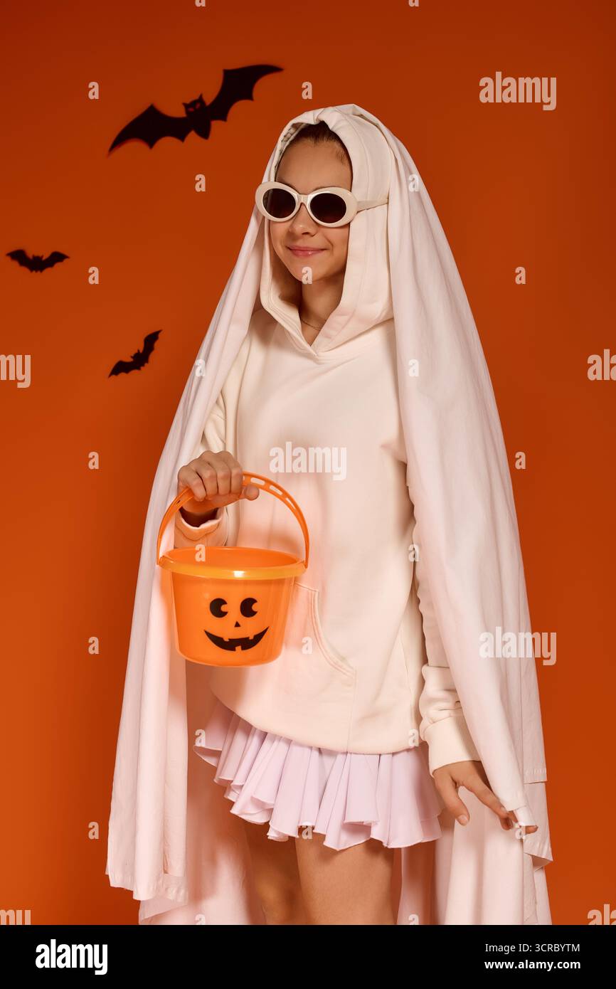 Una ragazza allegra vestita da fantasma ama le feste di Halloween su uno sfondo arancione. Foto Stock
