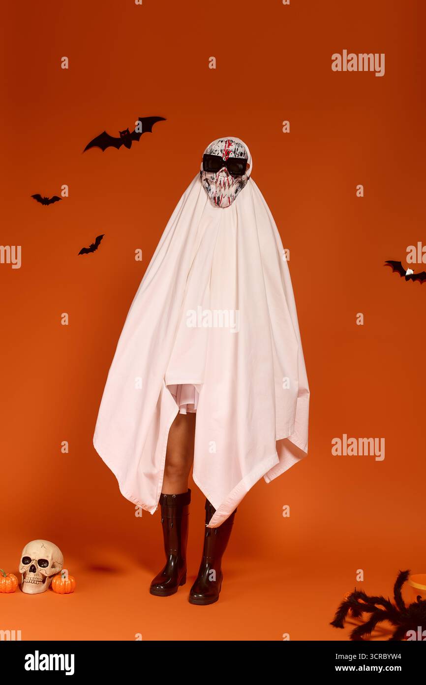 Un bambino celebra Halloween in un costume fantasma circondato da decorazioni festose. Foto Stock