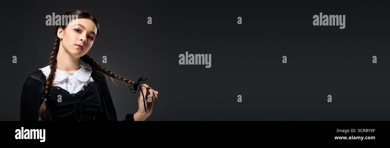 Una ragazza in costume gotico mercoledì con trecce pone con sicurezza per Halloween, striscione Foto Stock