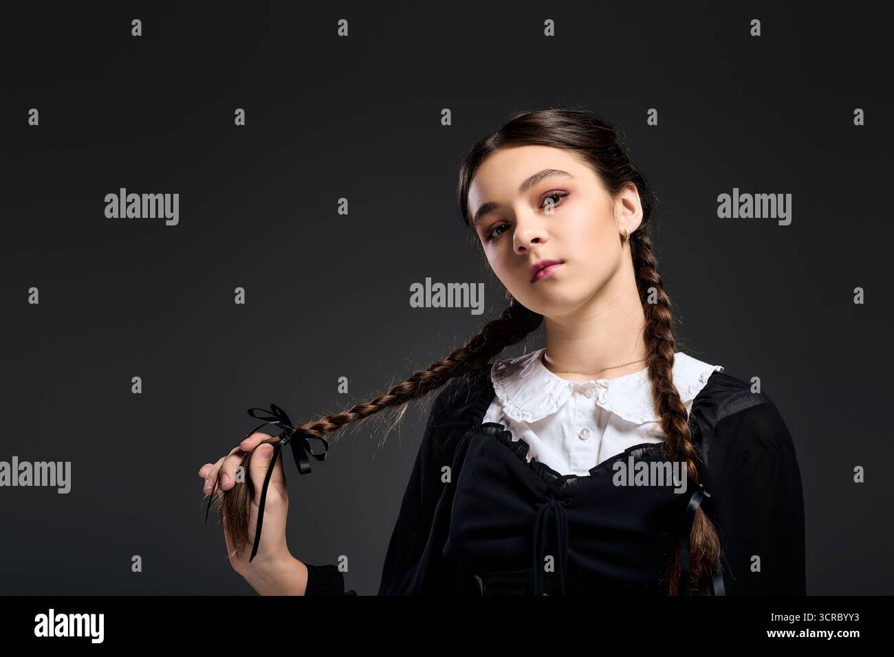 Una ragazza con trecce indossa un abito gotico di mercoledì, incarnando un personaggio spaventoso per Halloween. Foto Stock