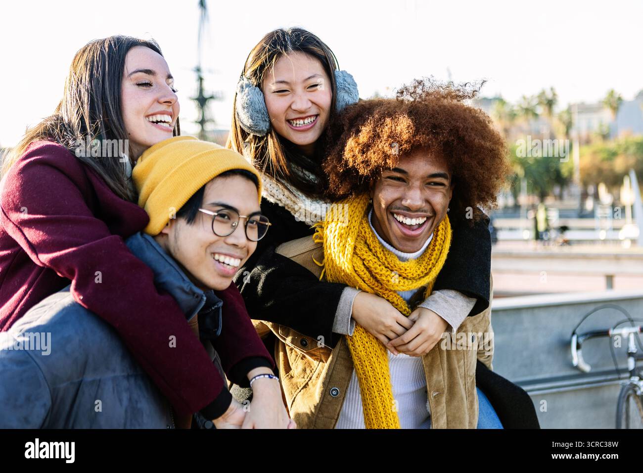 Amici multietnici felici che si divertono a fare il piggyback all'aperto in inverno Foto Stock