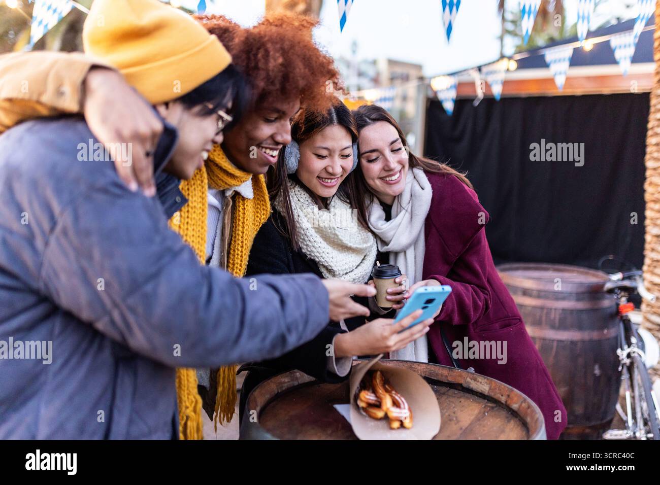 Amici multietnici felici che usano il telefono al mercatino di natale invernale Foto Stock