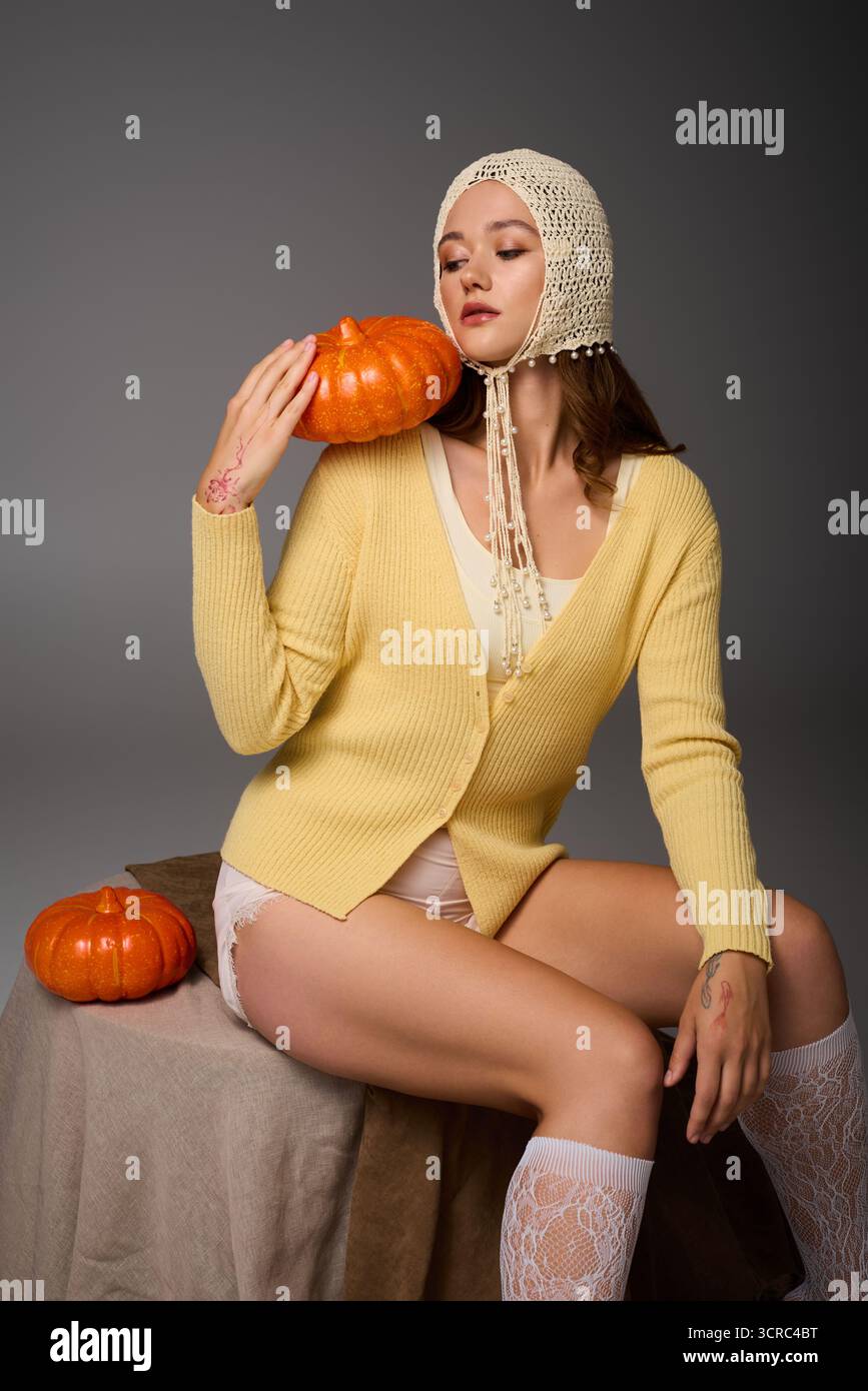 Una giovane donna con un abbigliamento elegante interagisce con le zucche, incarnando la moda autunnale e l'estro creativo. Foto Stock