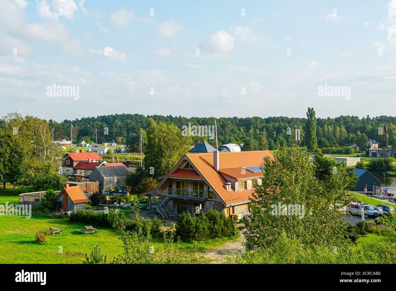 Pavilosta, Lettonia - 7 settembre 2025: Scenario pittoresco con una casa dal tetto rosso, giardini e vegetazione lussureggiante in un tranquillo villaggio rurale Foto Stock