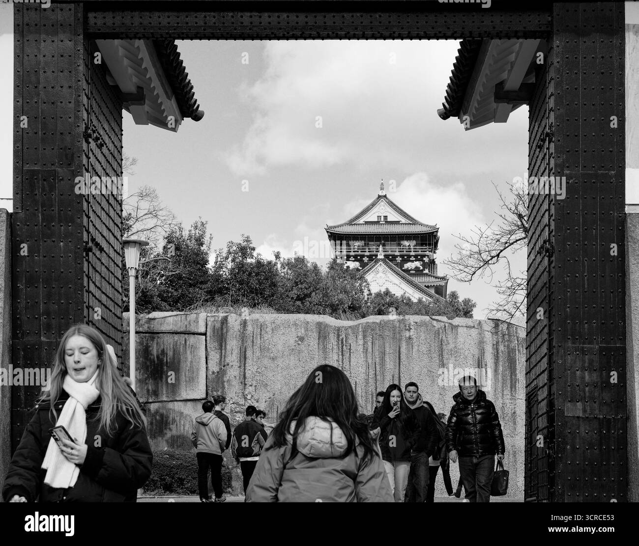 I visitatori camminano attraverso la grande porta del Castello di Osaka, con la torre principale incorniciata contro il cielo nuvoloso Foto Stock