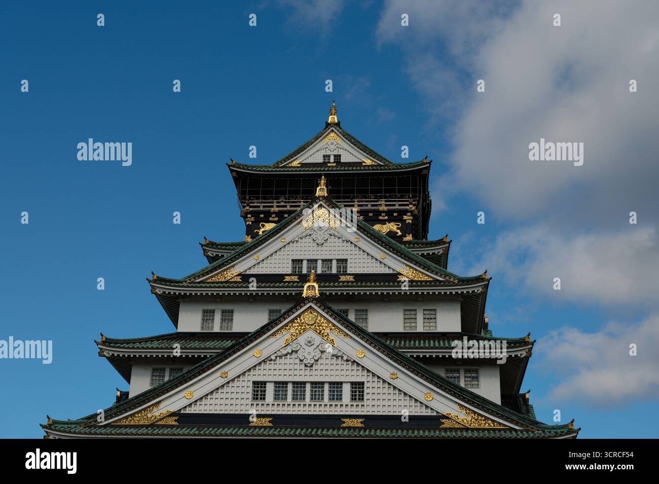 I piani superiori ornati del castello di Osaka, le sue pareti bianche, i tetti verdi e le decorazioni dorate che si distinguono contro il cielo Foto Stock