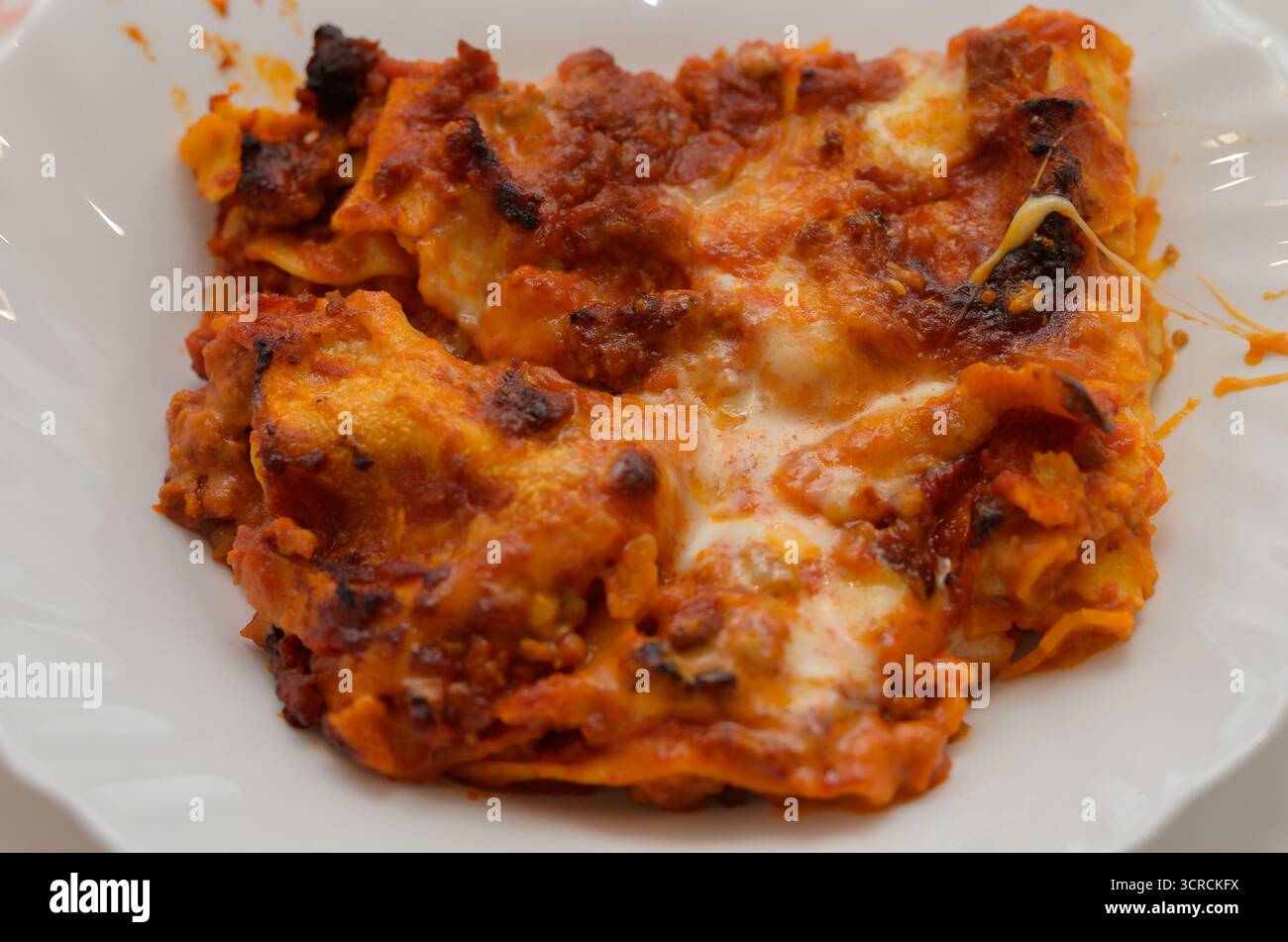 Un piatto di lasagne con formaggio e carne. Il piatto è a metà mangiato. La piastra è bianca e la lasagna è rossa Foto Stock