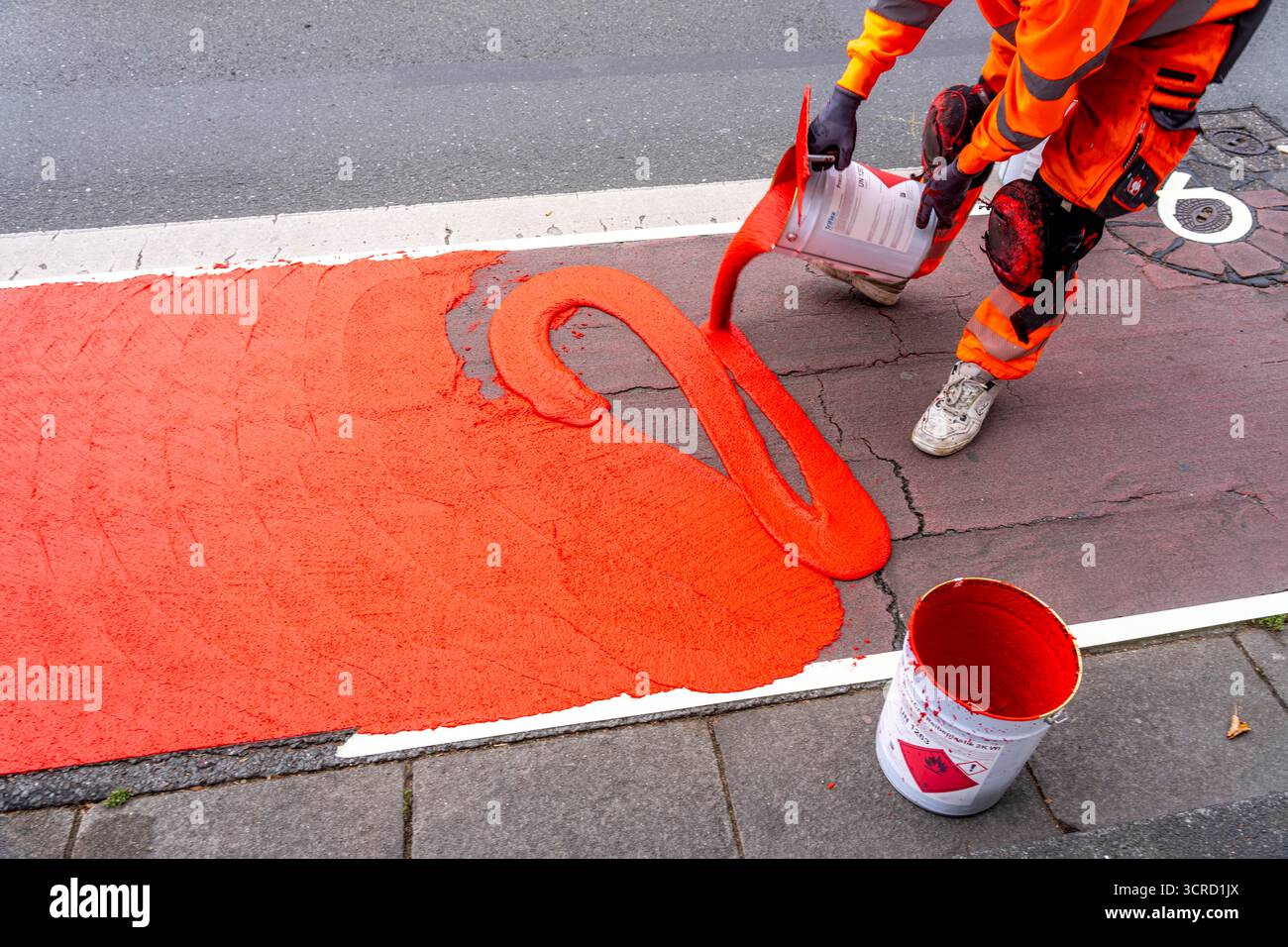 Applicazione della pavimentazione stradale rossa su una pista ciclabile, strada urbana, cosiddetta pavimentazione in plastica fredda, in rosso traffico, RAL3020. Il segno colorato è "i" Foto Stock