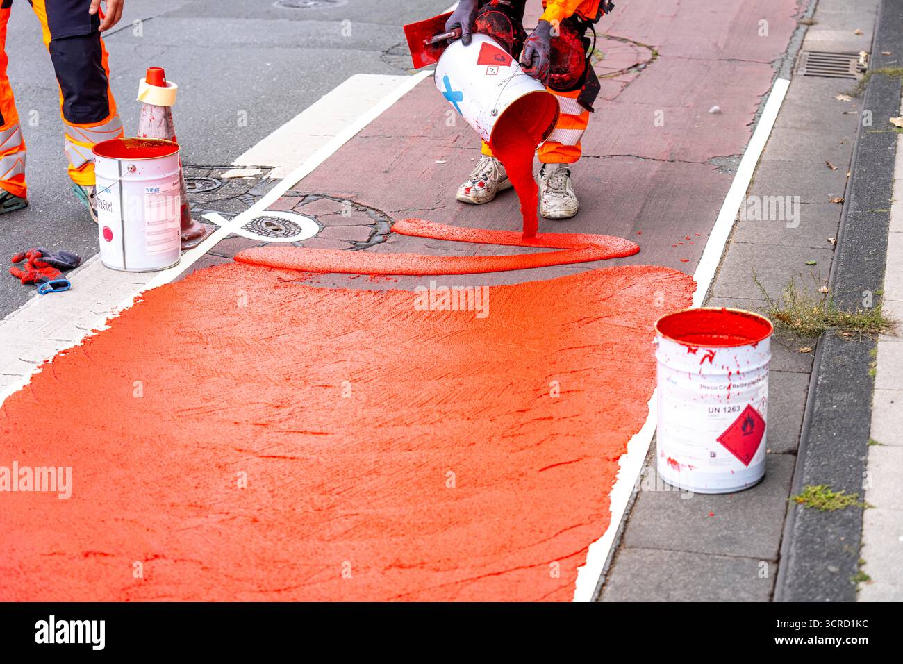 Applicazione della pavimentazione stradale rossa su una pista ciclabile, strada urbana, cosiddetta pavimentazione in plastica fredda, in rosso traffico, RAL3020. Il segno colorato è "i" Foto Stock