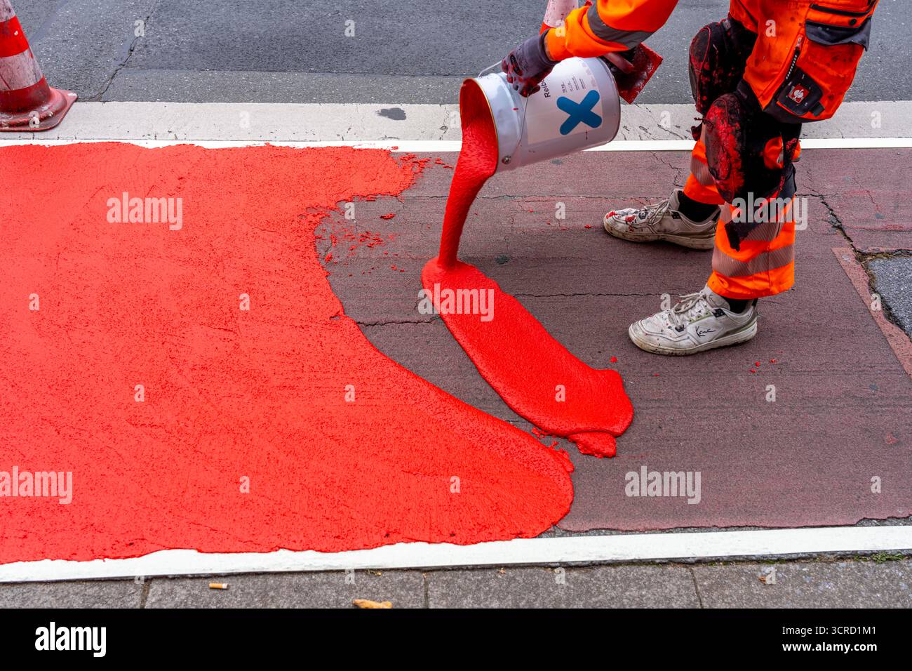 Applicazione della pavimentazione stradale rossa su una pista ciclabile, strada urbana, cosiddetta pavimentazione in plastica fredda, in rosso traffico, RAL3020. Il segno colorato è "i" Foto Stock