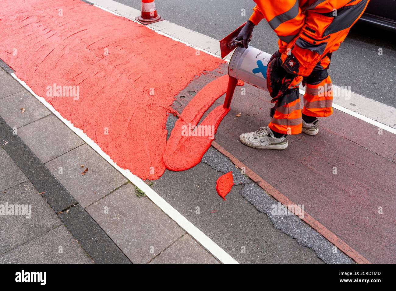 Applicazione della pavimentazione stradale rossa su una pista ciclabile, strada urbana, cosiddetta pavimentazione in plastica fredda, in rosso traffico, RAL3020. Il segno colorato è "i" Foto Stock