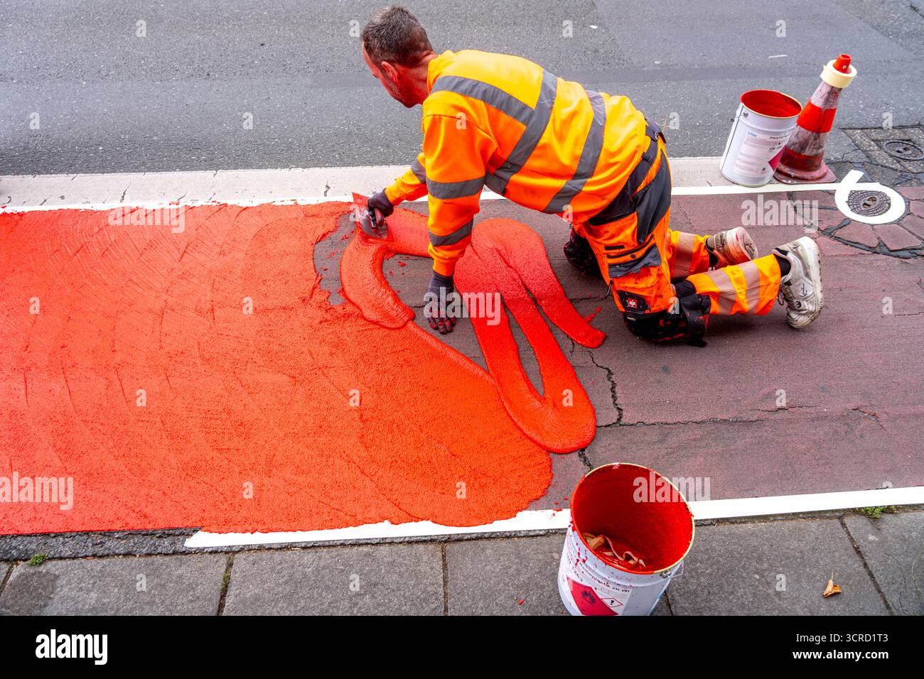 Applicazione della pavimentazione stradale rossa su una pista ciclabile, strada urbana, cosiddetta pavimentazione in plastica fredda, in rosso traffico, RAL3020. Il segno colorato è "i" Foto Stock