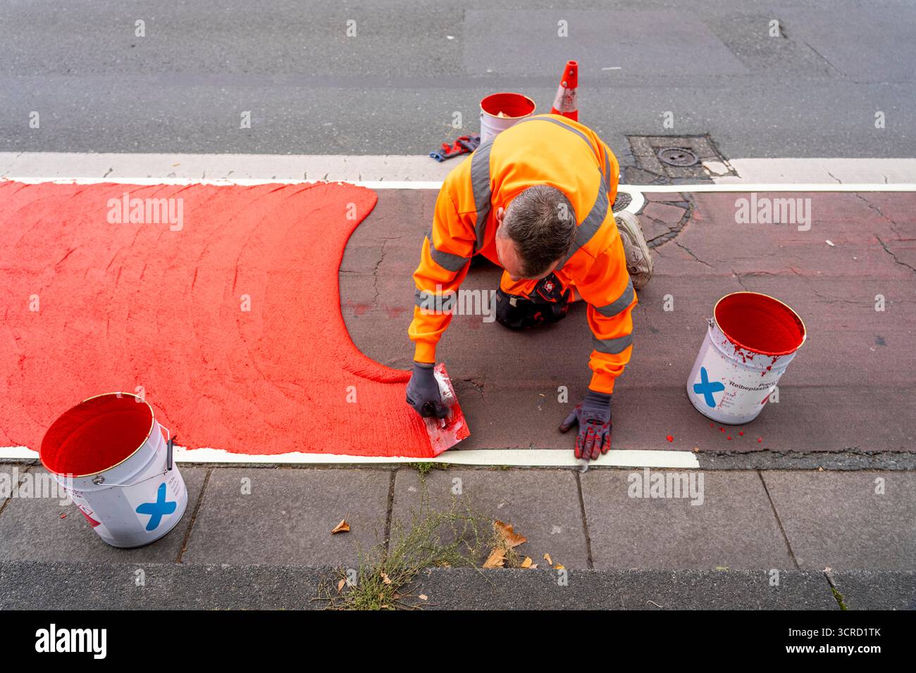 Applicazione della pavimentazione stradale rossa su una pista ciclabile, strada urbana, cosiddetta pavimentazione in plastica fredda, in rosso traffico, RAL3020. Il segno colorato è "i" Foto Stock