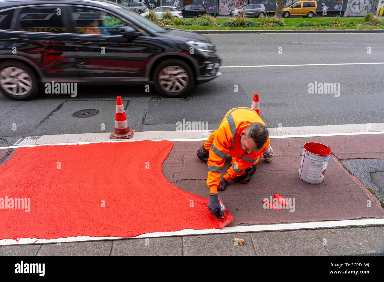 Applicazione della pavimentazione stradale rossa su una pista ciclabile, strada urbana, cosiddetta pavimentazione in plastica fredda, in rosso traffico, RAL3020. Il segno colorato è "i" Foto Stock