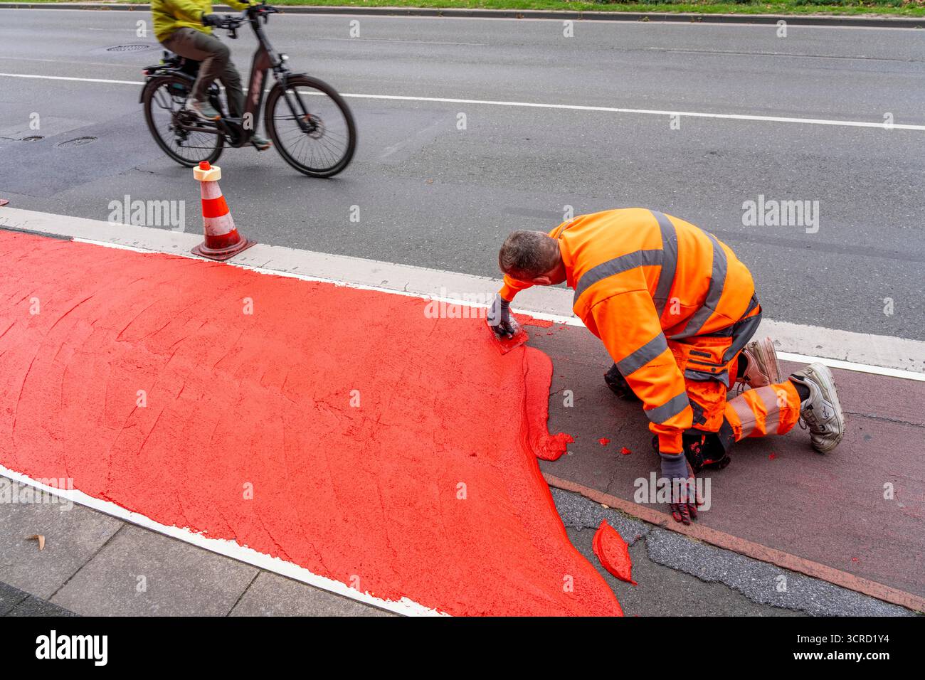 Applicazione della pavimentazione stradale rossa su una pista ciclabile, strada urbana, cosiddetta pavimentazione in plastica fredda, in rosso traffico, RAL3020. Il segno colorato è "i" Foto Stock