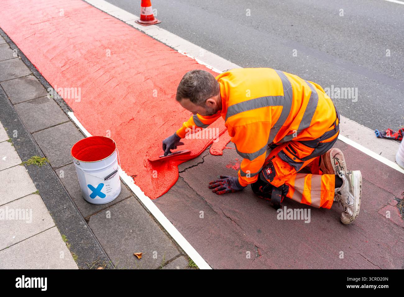 Applicazione della pavimentazione stradale rossa su una pista ciclabile, strada urbana, cosiddetta pavimentazione in plastica fredda, in rosso traffico, RAL3020. Il segno colorato è "i" Foto Stock
