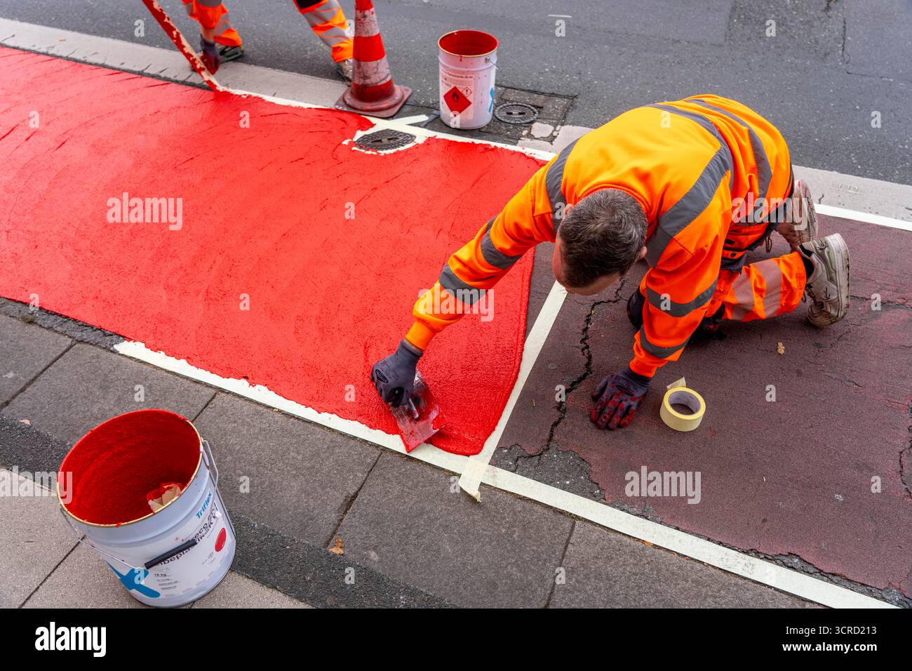 Applicazione della pavimentazione stradale rossa su una pista ciclabile, strada urbana, cosiddetta pavimentazione in plastica fredda, in rosso traffico, RAL3020. Il segno colorato è "i" Foto Stock
