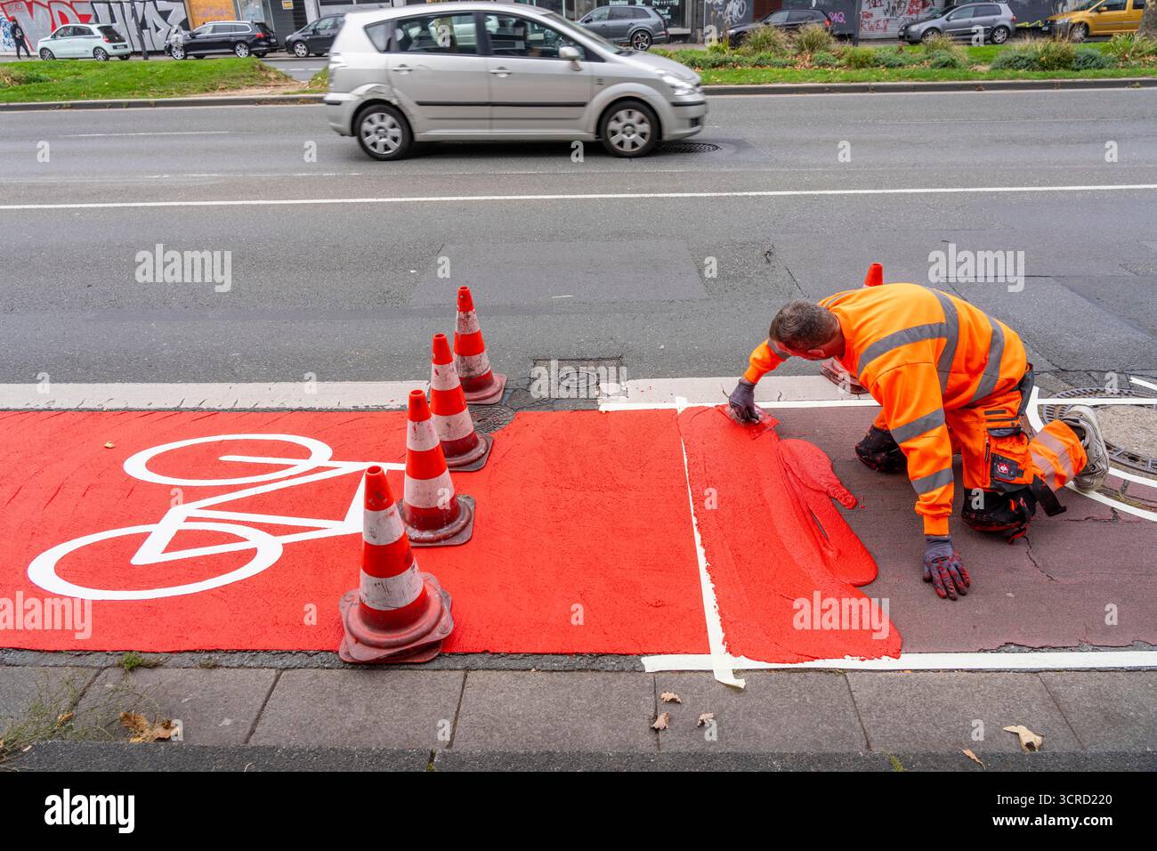 Applicazione della pavimentazione stradale rossa su una pista ciclabile, strada urbana, cosiddetta pavimentazione in plastica fredda, in rosso traffico, RAL3020. Il segno colorato è "i" Foto Stock