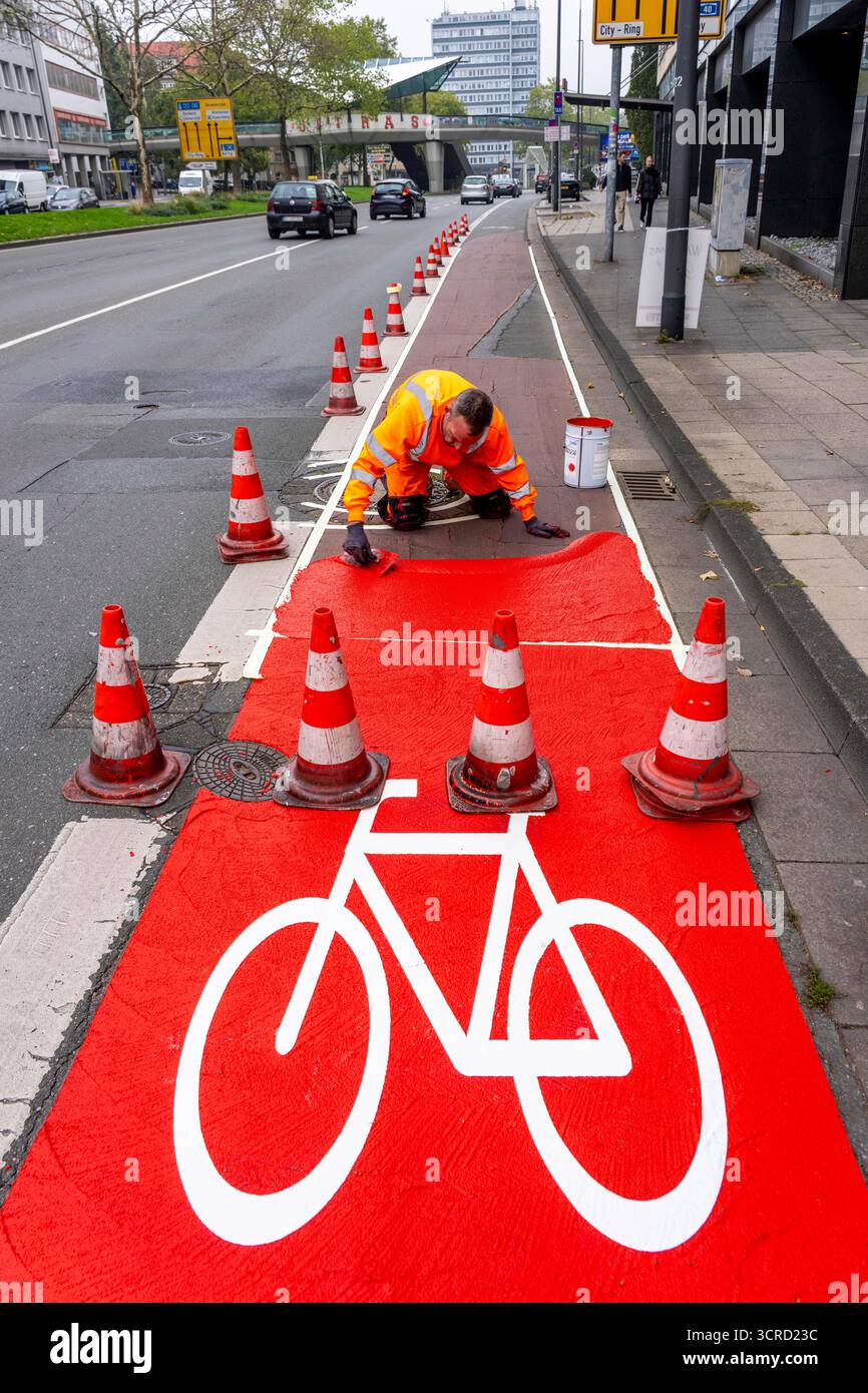 Applicazione della pavimentazione stradale rossa su una pista ciclabile, strada urbana, cosiddetta pavimentazione in plastica fredda, in rosso traffico, RAL3020. Il segno colorato è "i" Foto Stock