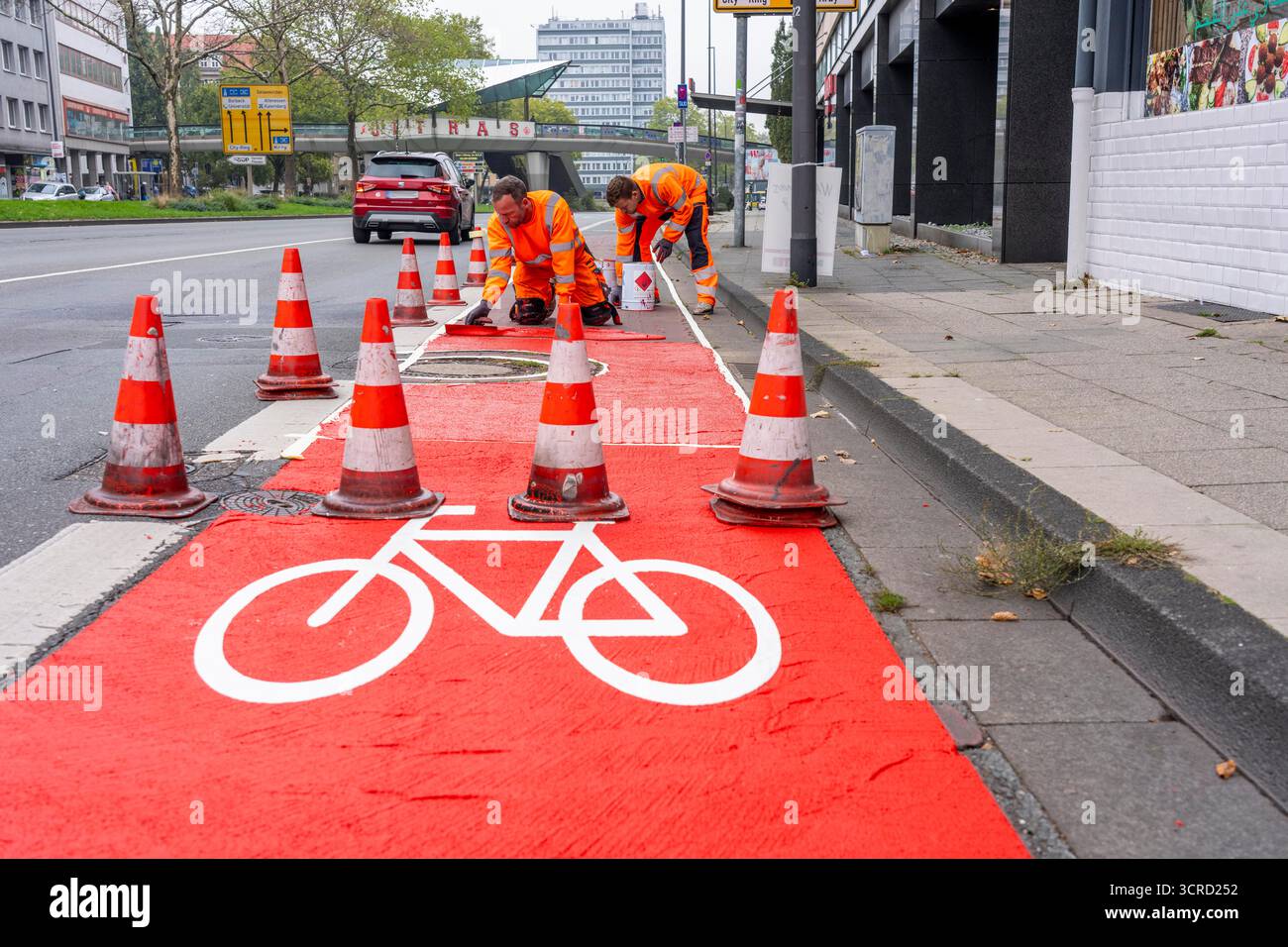 Applicazione della pavimentazione stradale rossa su una pista ciclabile, strada urbana, cosiddetta pavimentazione in plastica fredda, in rosso traffico, RAL3020. Il segno colorato è "i" Foto Stock