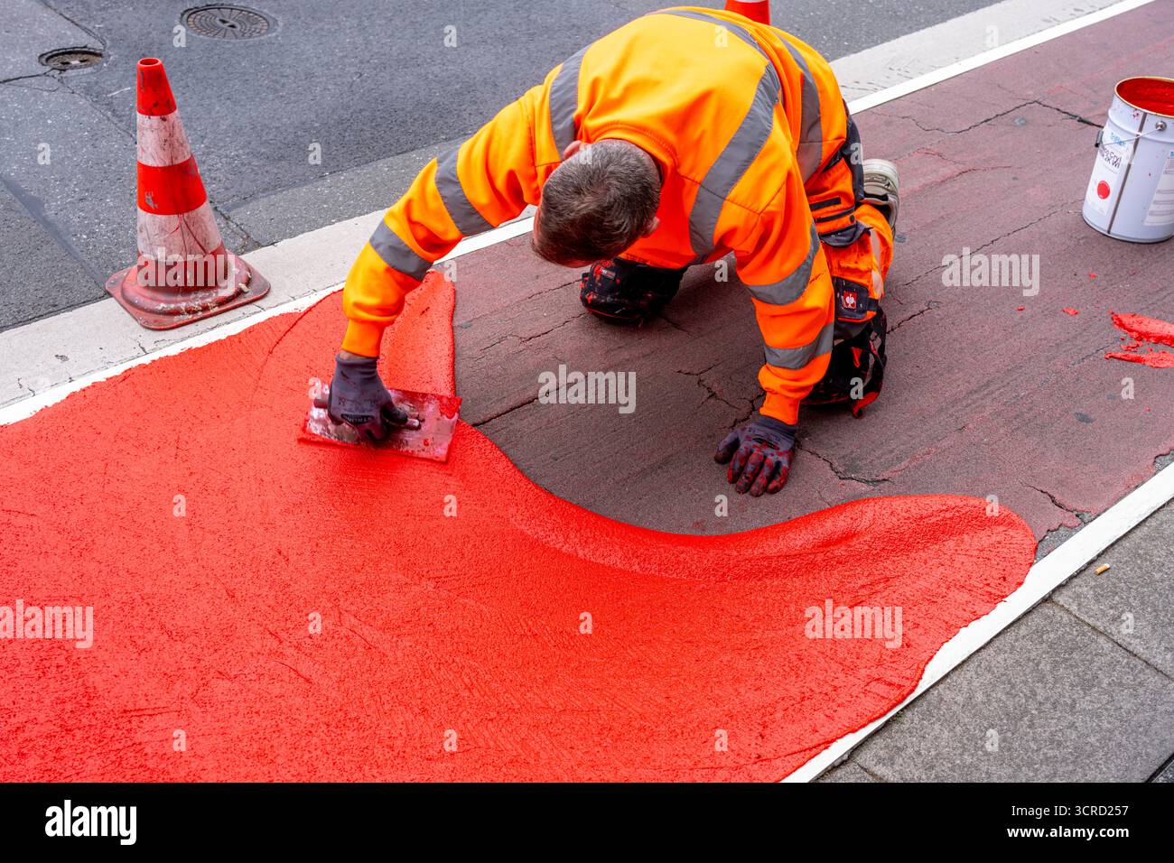 Applicazione della pavimentazione stradale rossa su una pista ciclabile, strada urbana, cosiddetta pavimentazione in plastica fredda, in rosso traffico, RAL3020. Il segno colorato è "i" Foto Stock