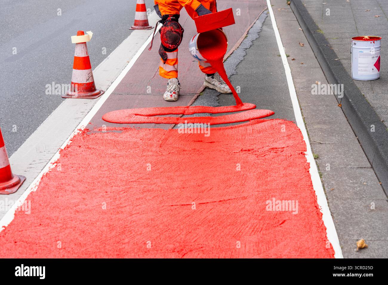 Applicazione della pavimentazione stradale rossa su una pista ciclabile, strada urbana, cosiddetta pavimentazione in plastica fredda, in rosso traffico, RAL3020. Il segno colorato è "i" Foto Stock