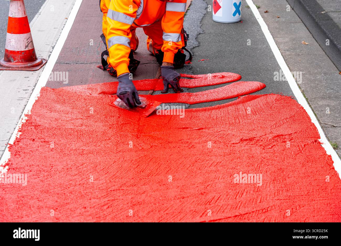 Applicazione della pavimentazione stradale rossa su una pista ciclabile, strada urbana, cosiddetta pavimentazione in plastica fredda, in rosso traffico, RAL3020. Il segno colorato è "i" Foto Stock