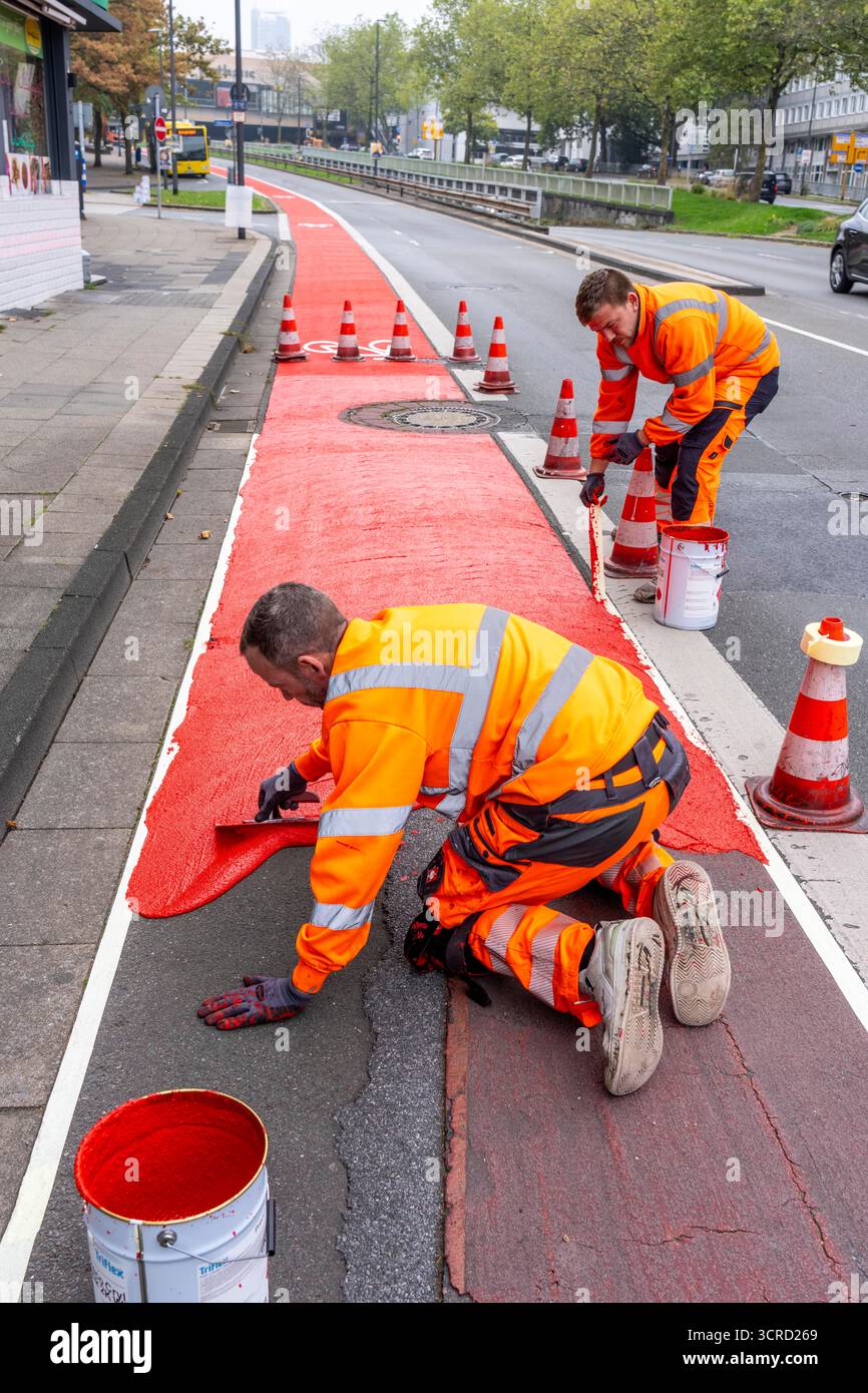 Applicazione della pavimentazione stradale rossa su una pista ciclabile, strada urbana, cosiddetta pavimentazione in plastica fredda, in rosso traffico, RAL3020. Il segno colorato è "i" Foto Stock