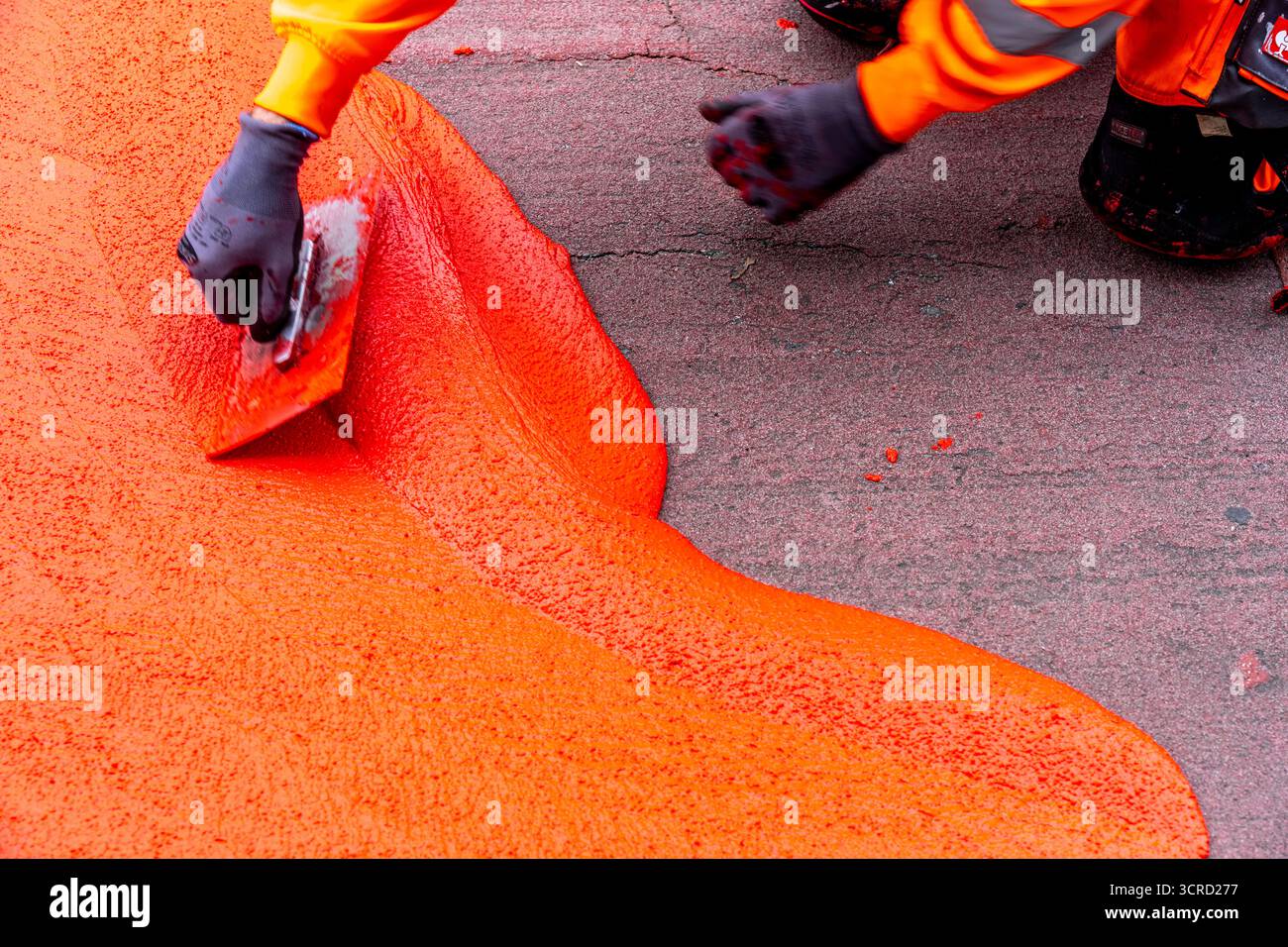 Applicazione della pavimentazione stradale rossa su una pista ciclabile, strada urbana, cosiddetta pavimentazione in plastica fredda, in rosso traffico, RAL3020. Il segno colorato è "i" Foto Stock