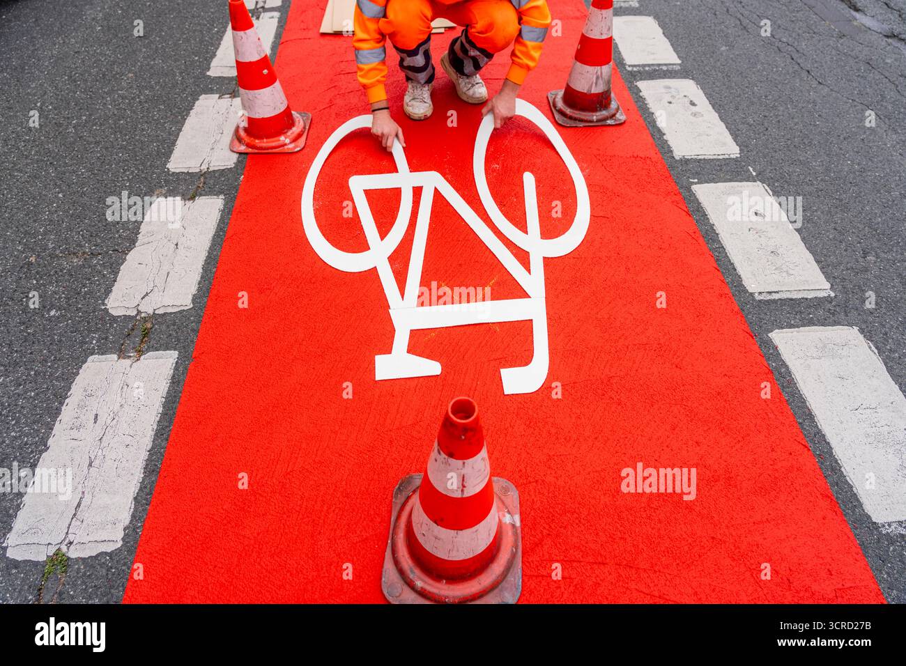 Applicazione della pavimentazione stradale rossa su una pista ciclabile, strada urbana, cosiddetta pavimentazione in plastica fredda, in rosso traffico, RAL3020. Il segno colorato è "i" Foto Stock