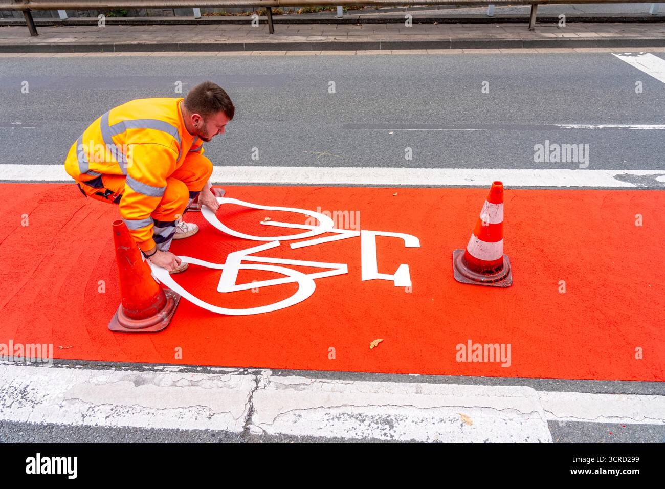 Applicazione della pavimentazione stradale rossa su una pista ciclabile, strada urbana, cosiddetta pavimentazione in plastica fredda, in rosso traffico, RAL3020. Il segno colorato è "i" Foto Stock