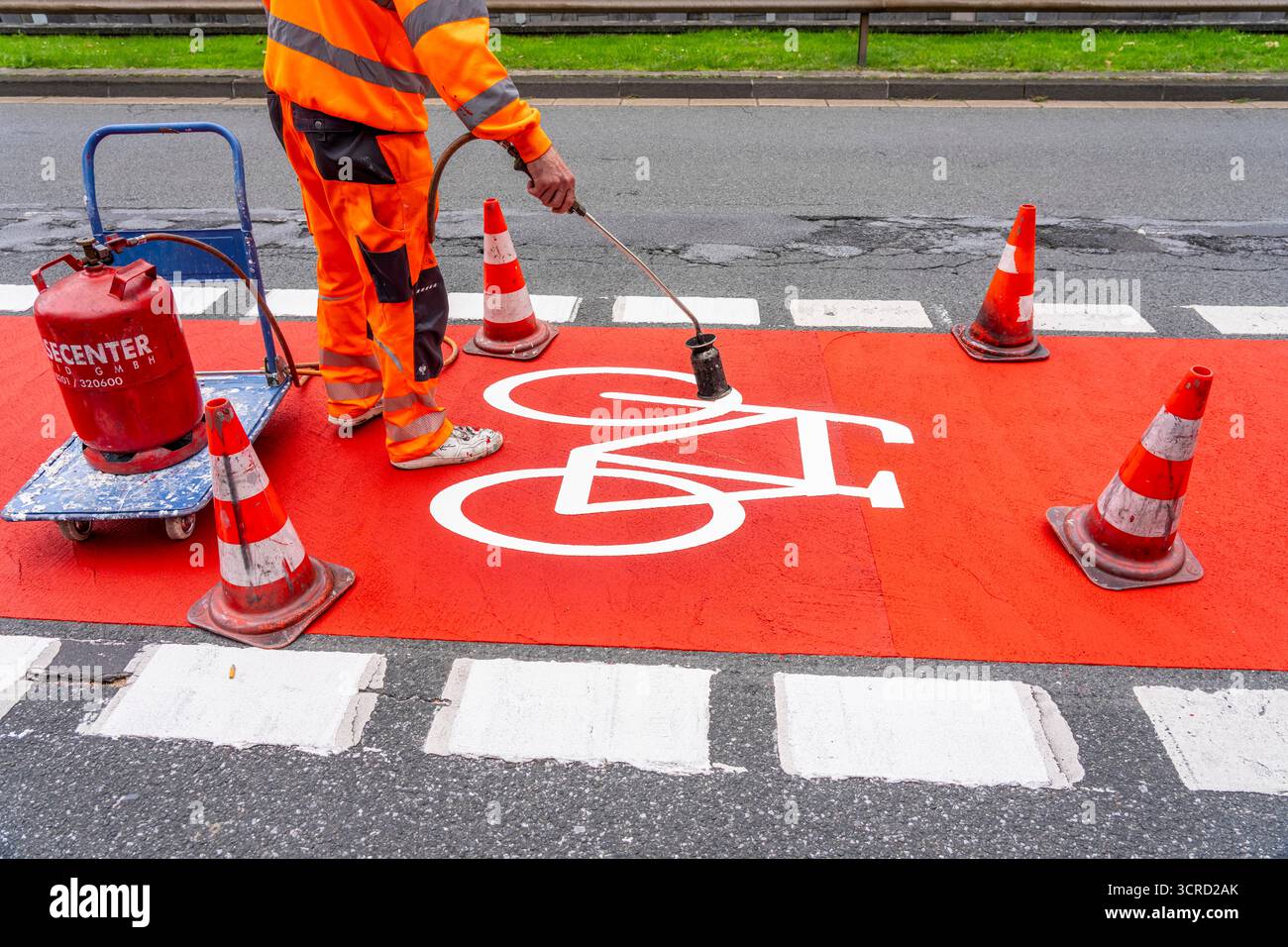 Applicazione della pavimentazione stradale rossa su una pista ciclabile, strada urbana, cosiddetta pavimentazione in plastica fredda, in rosso traffico, RAL3020. Il segno colorato è "i" Foto Stock