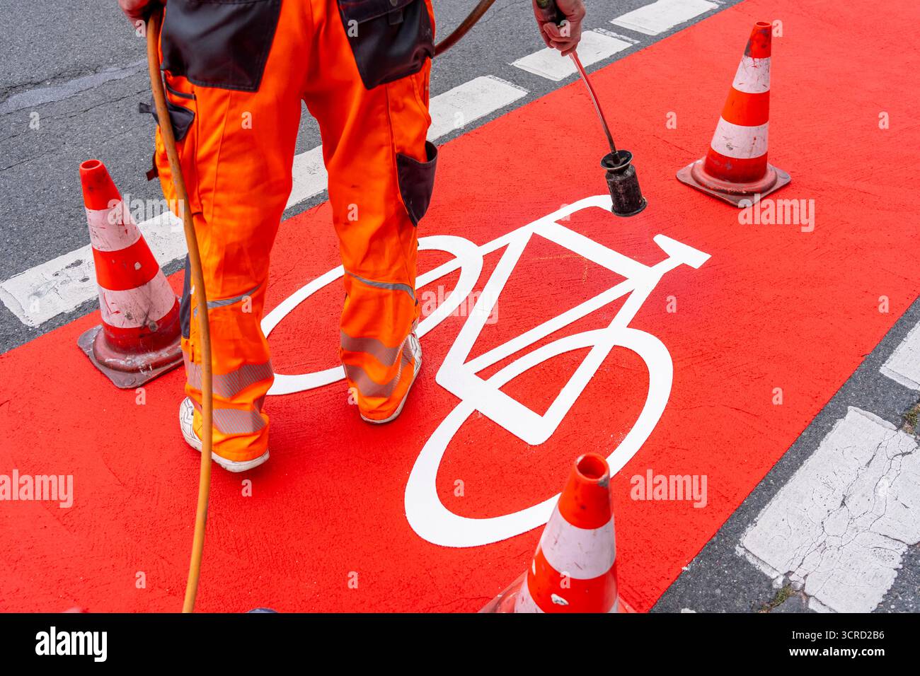 Applicazione della pavimentazione stradale rossa su una pista ciclabile, strada urbana, cosiddetta pavimentazione in plastica fredda, in rosso traffico, RAL3020. Il segno colorato è "i" Foto Stock
