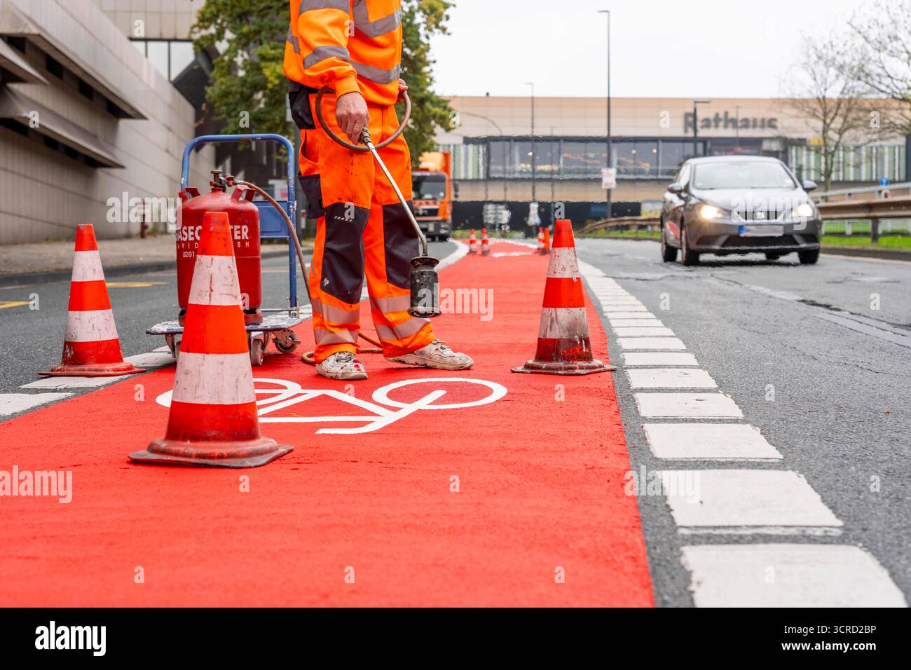 Applicazione della pavimentazione stradale rossa su una pista ciclabile, strada urbana, cosiddetta pavimentazione in plastica fredda, in rosso traffico, RAL3020. Il segno colorato è "i" Foto Stock