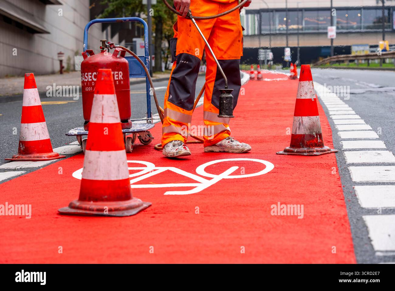 Applicazione della pavimentazione stradale rossa su una pista ciclabile, strada urbana, cosiddetta pavimentazione in plastica fredda, in rosso traffico, RAL3020. Il segno colorato è "i" Foto Stock