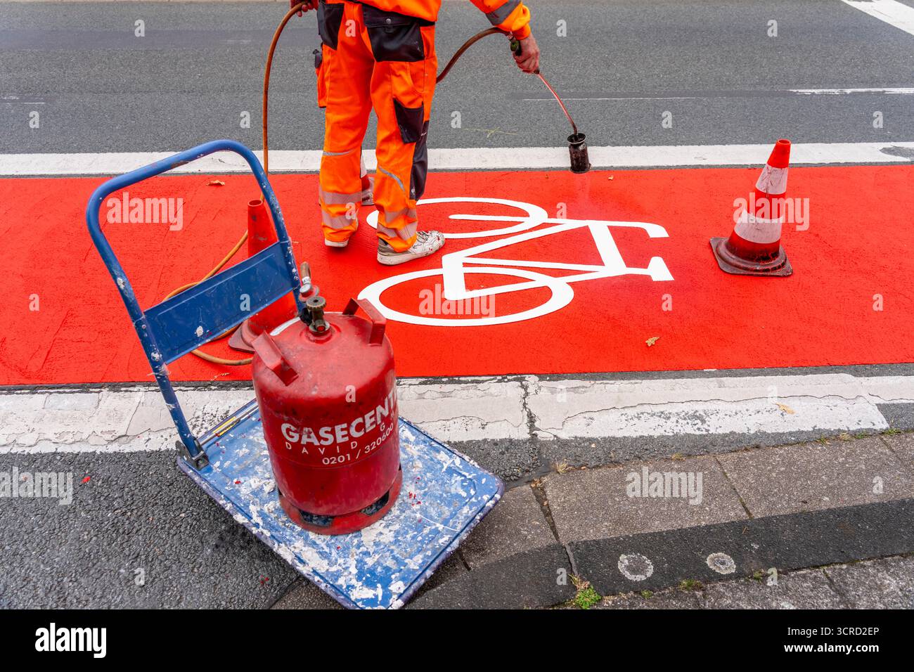 Applicazione della pavimentazione stradale rossa su una pista ciclabile, strada urbana, cosiddetta pavimentazione in plastica fredda, in rosso traffico, RAL3020. Il segno colorato è "i" Foto Stock