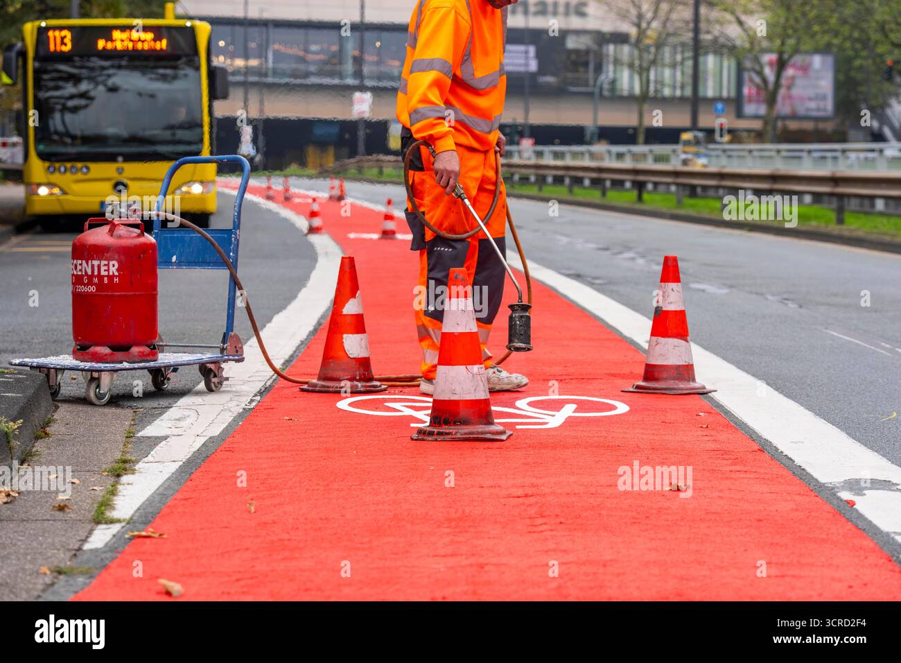 Applicazione della pavimentazione stradale rossa su una pista ciclabile, strada urbana, cosiddetta pavimentazione in plastica fredda, in rosso traffico, RAL3020. Il segno colorato è "i" Foto Stock