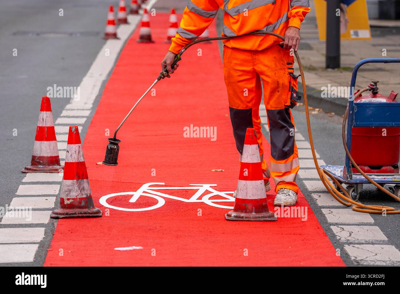 Applicazione della pavimentazione stradale rossa su una pista ciclabile, strada urbana, cosiddetta pavimentazione in plastica fredda, in rosso traffico, RAL3020. Il segno colorato è "i" Foto Stock