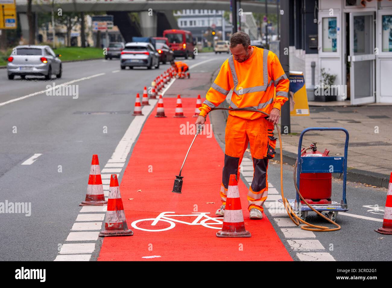 Applicazione della pavimentazione stradale rossa su una pista ciclabile, strada urbana, cosiddetta pavimentazione in plastica fredda, in rosso traffico, RAL3020. Il segno colorato è "i" Foto Stock