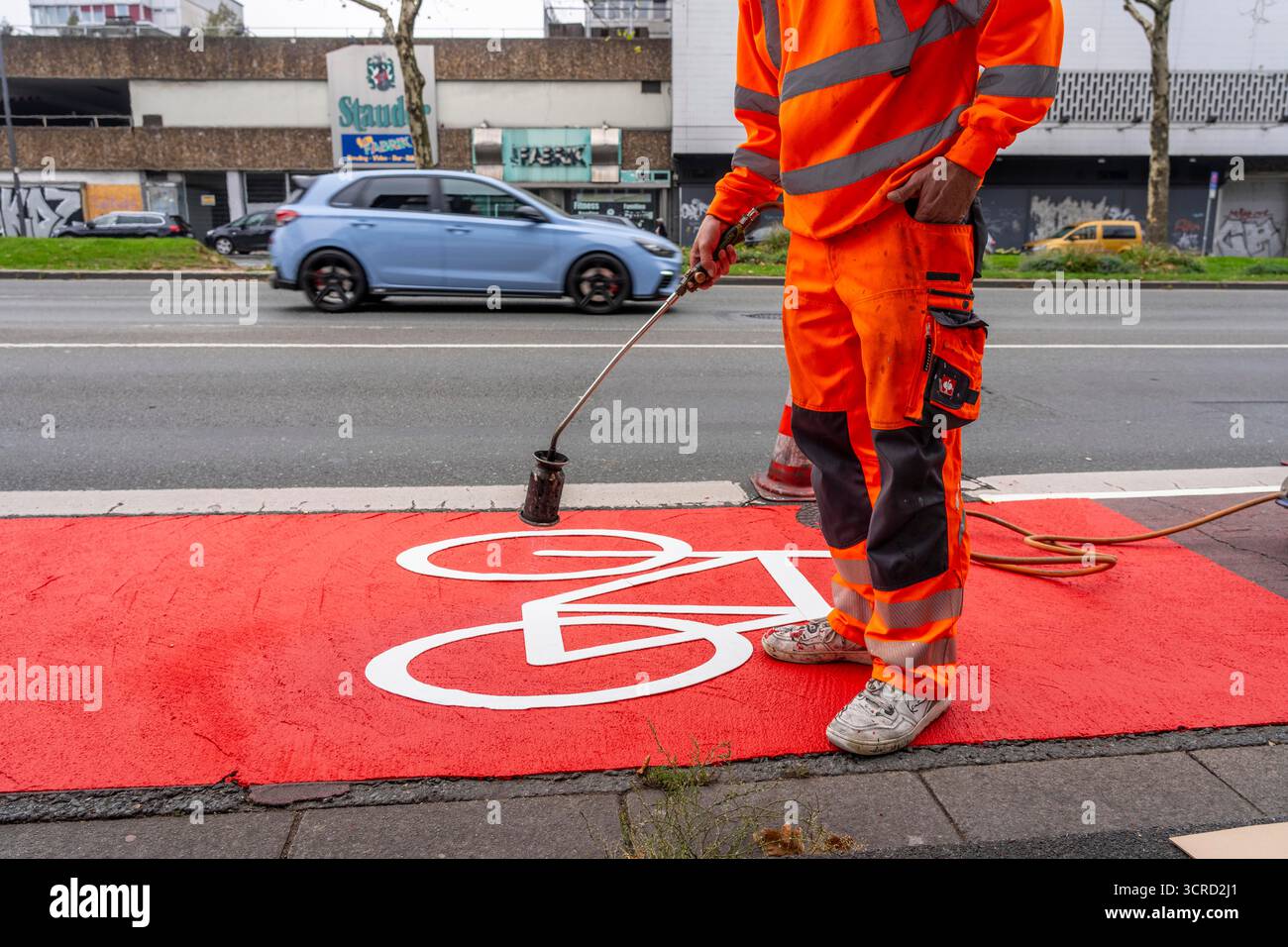 Applicazione della pavimentazione stradale rossa su una pista ciclabile, strada urbana, cosiddetta pavimentazione in plastica fredda, in rosso traffico, RAL3020. Il segno colorato è "i" Foto Stock