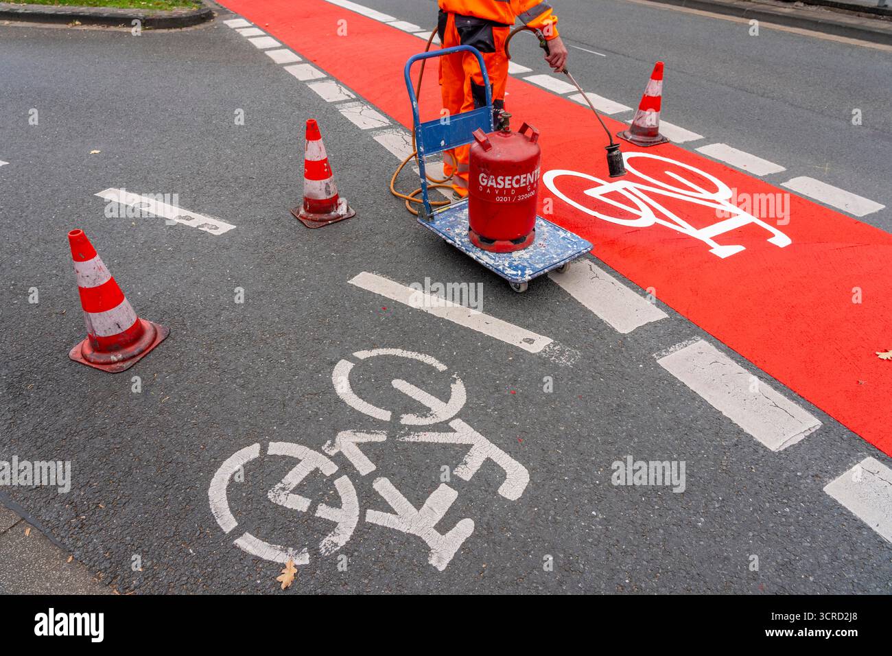 Applicazione della pavimentazione stradale rossa su una pista ciclabile, strada urbana, cosiddetta pavimentazione in plastica fredda, in rosso traffico, RAL3020. Il segno colorato è "i" Foto Stock