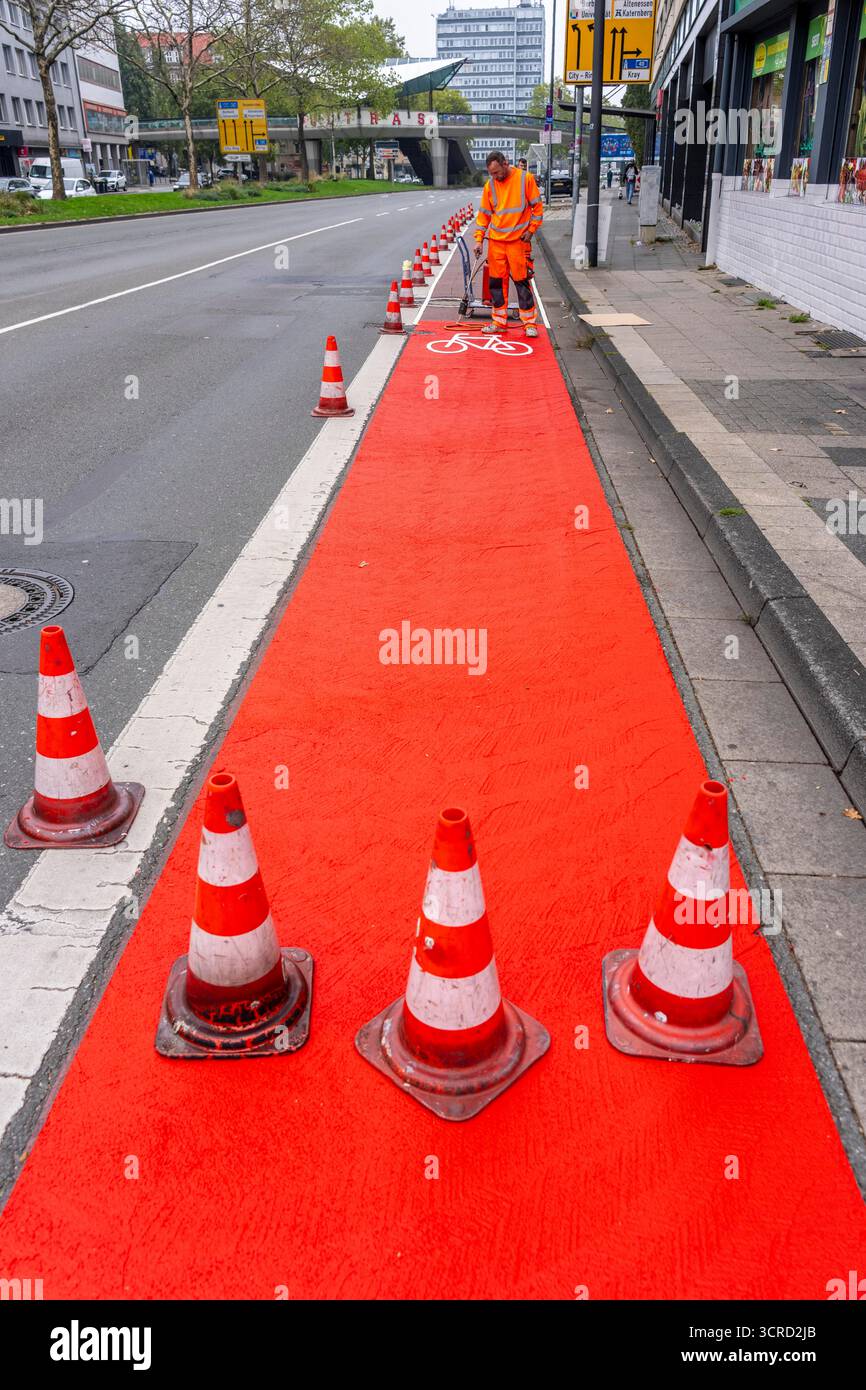 Applicazione della pavimentazione stradale rossa su una pista ciclabile, strada urbana, cosiddetta pavimentazione in plastica fredda, in rosso traffico, RAL3020. Il segno colorato è "i" Foto Stock
