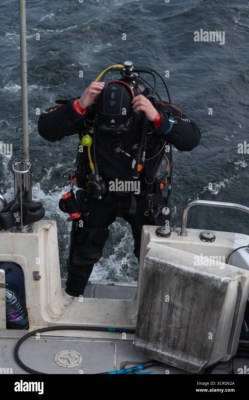 Mare di Barents, Russia - 14 giugno 2025: Subacqueo in muta asciutta e carro armato si appoggia in avanti sul bordo della barca Foto Stock