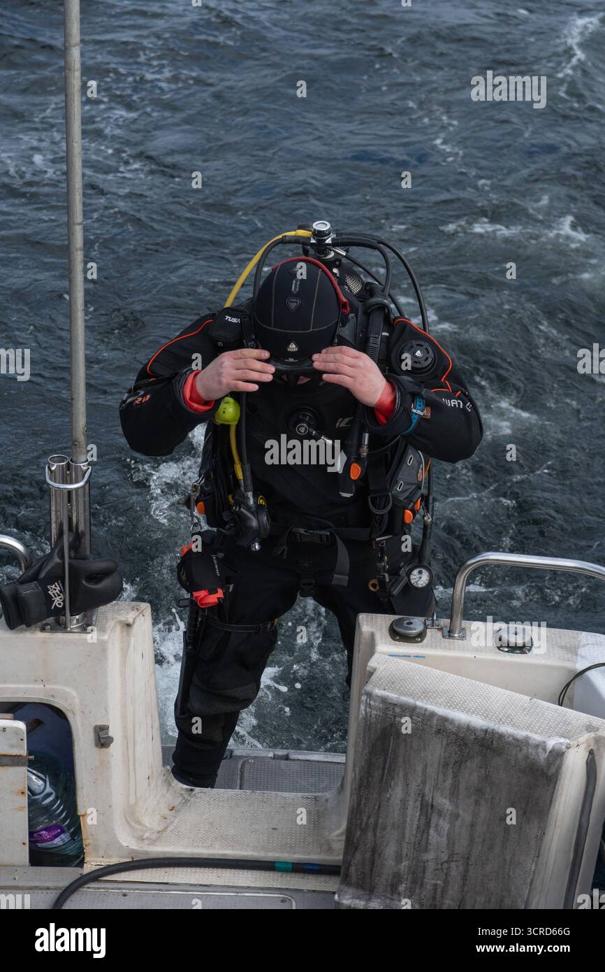 Mare di Barents, Russia - 14 giugno 2025: Subacqueo in tuta nera asciutta si prepara all'esplorazione subacquea dal ponte della barca Foto Stock