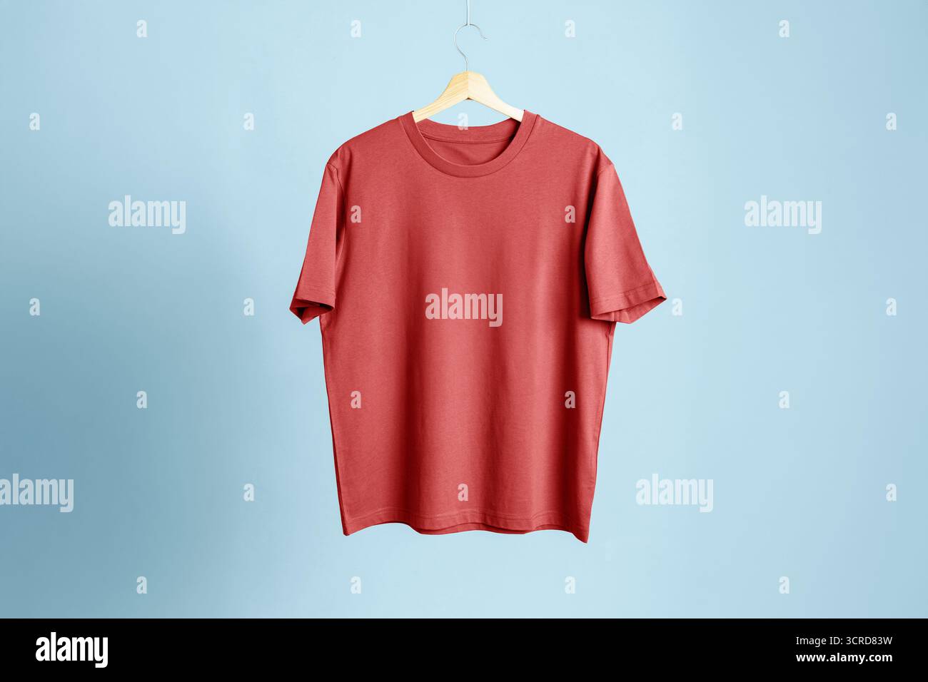 T-shirt rossa (corallo) di cotone di altissima qualità appesa su un gancio di legno. Mockup isolato su sfondo blu neutro. Perfetto per il negozio online Foto Stock