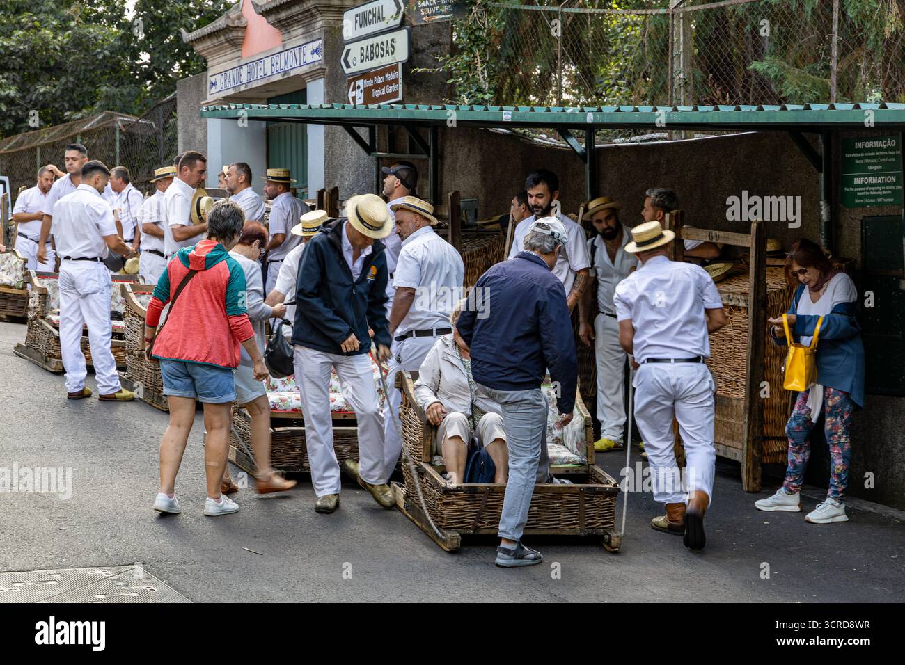 I turisti si preparano a cavalcare i tradizionali toboga in vimini con guide locali in uniforme bianca in una strada a Funchal, Madeira Foto Stock